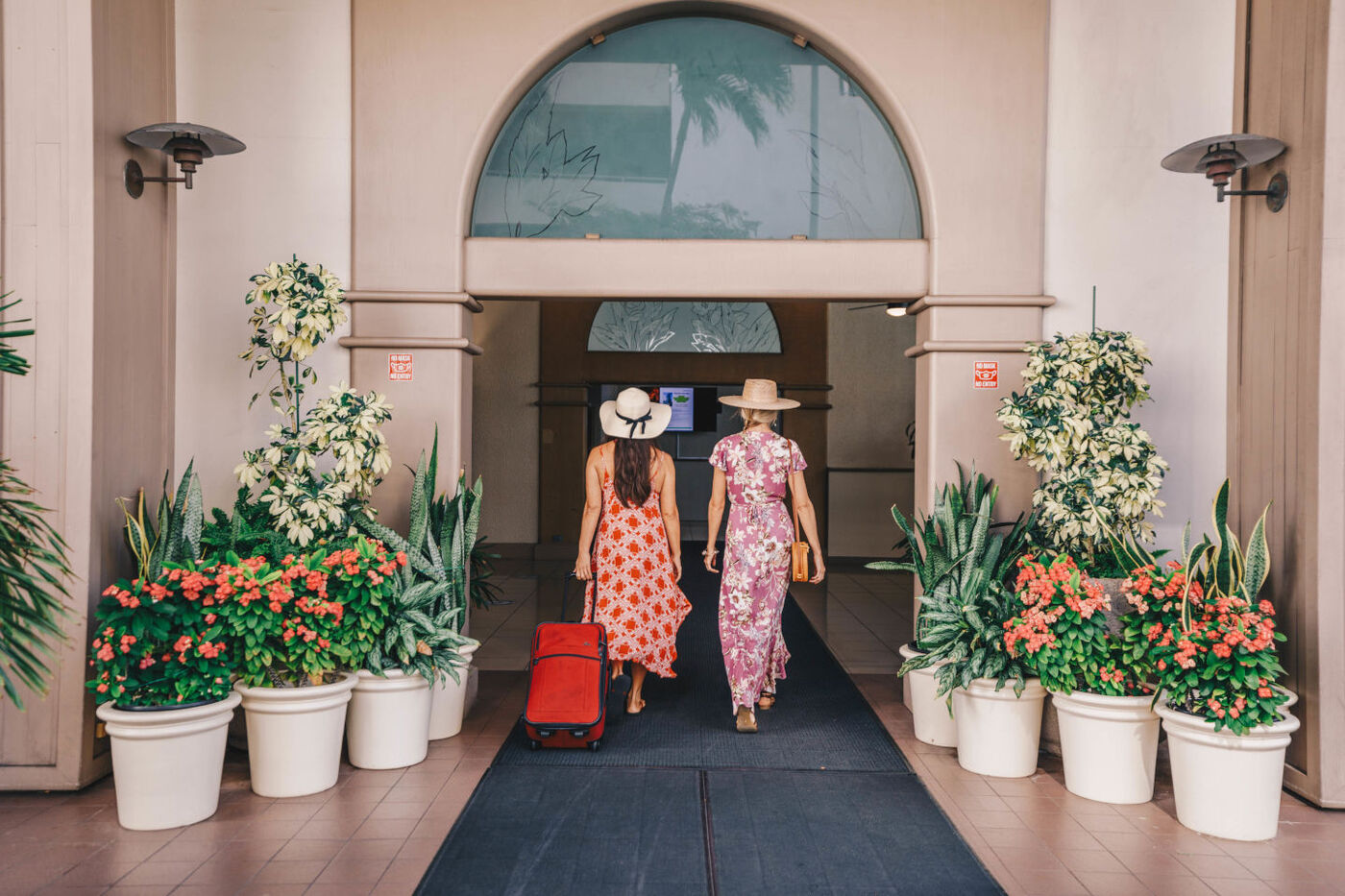 Two ladies wearing floral printed dresses enter the Aston Waikiki Sunset with their luggage in tow.