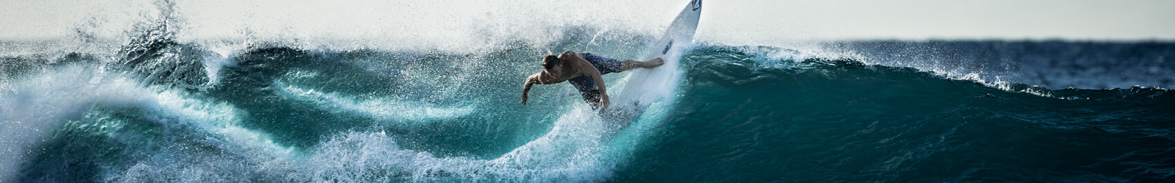 Surfer wearing blue surf shorts on a white surfboard surfing on a wave in the crystal blue water