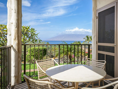 Balcony with table, chairs, and views of ocean and neighbor island.