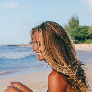 Andrea Hanneman side view smiling sitting on the sand at the beach