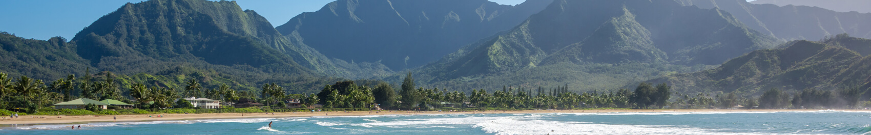 Shoreline at a beach along Kauai's North Shore with a white house to the left and mountains in the background