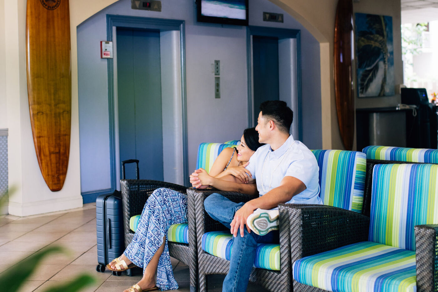 Lobby seating area with couple sitting enjoying the comfortable chairs near the elevators and the iconic surf boards hanging on the wall