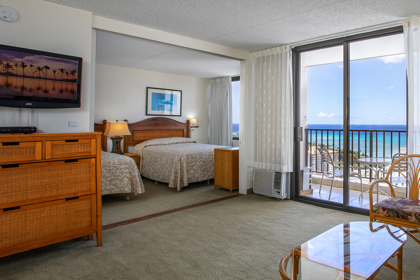 Living area with two beds, coffee table, TV, and balcony.