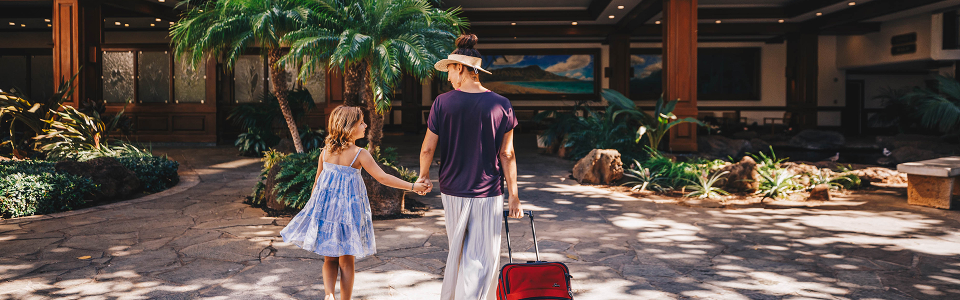 Daughter and mother walking through hotel entrance with luggage
