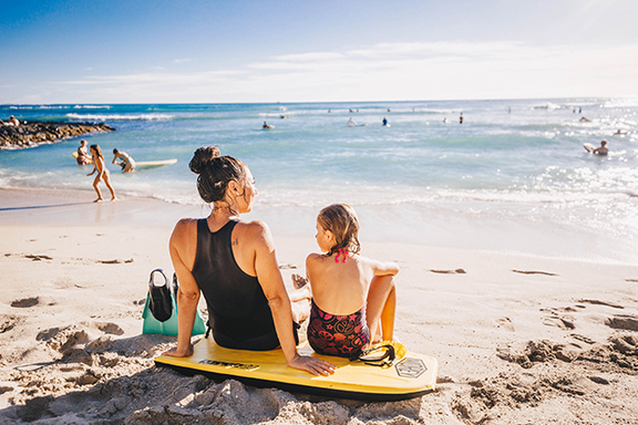 Woman and girl sitting on the beach with boogie board