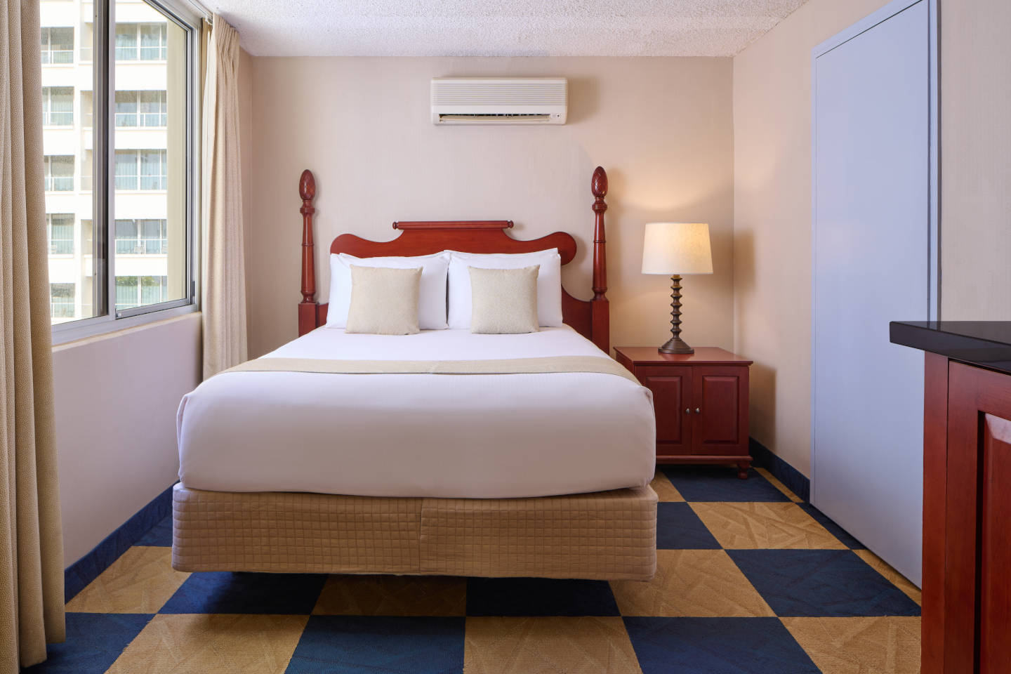 Moderate Hotel Room with queen bed configuration and nightstand with lamp