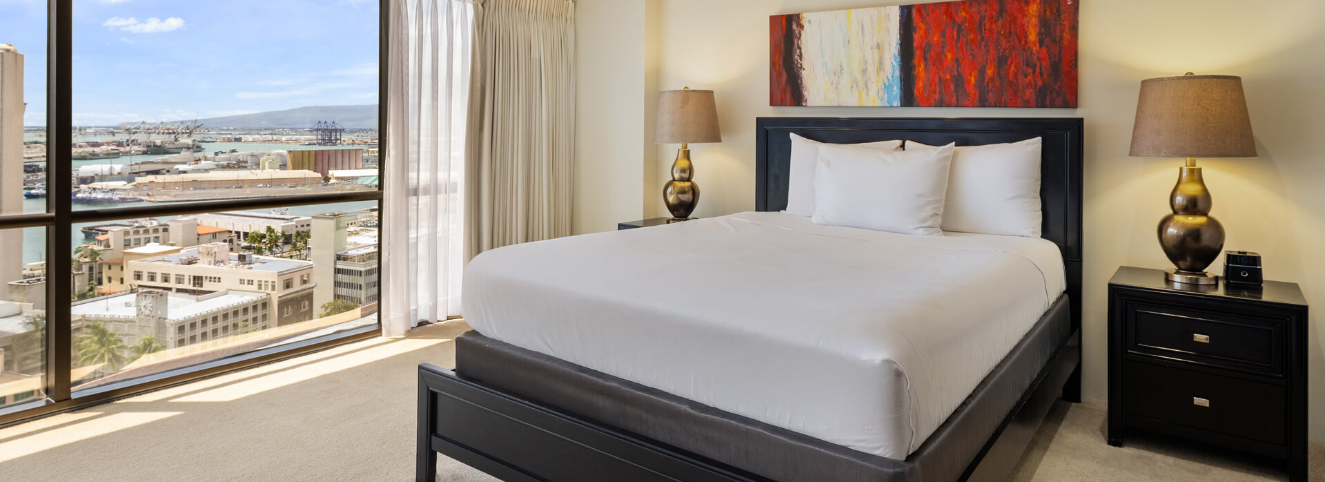 Room with large windows and view of ocean, a bed, nightstand, and lamps.