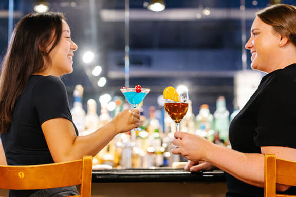 2 women enjoying cocktails at bar