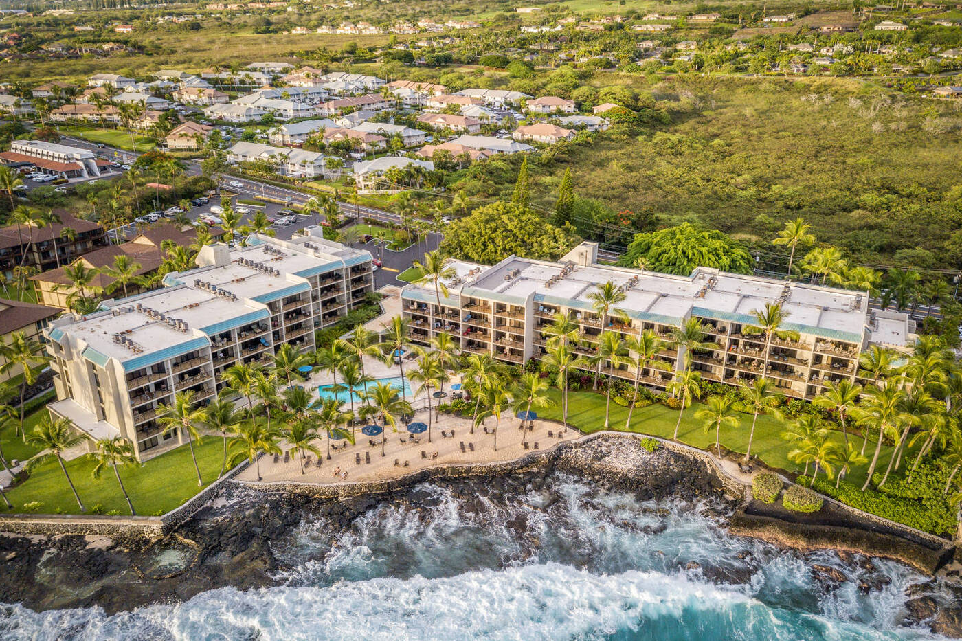 Aerial view of Aston Kona by the Sea lined by black lava rocks, coconut tress, and blue ocean
