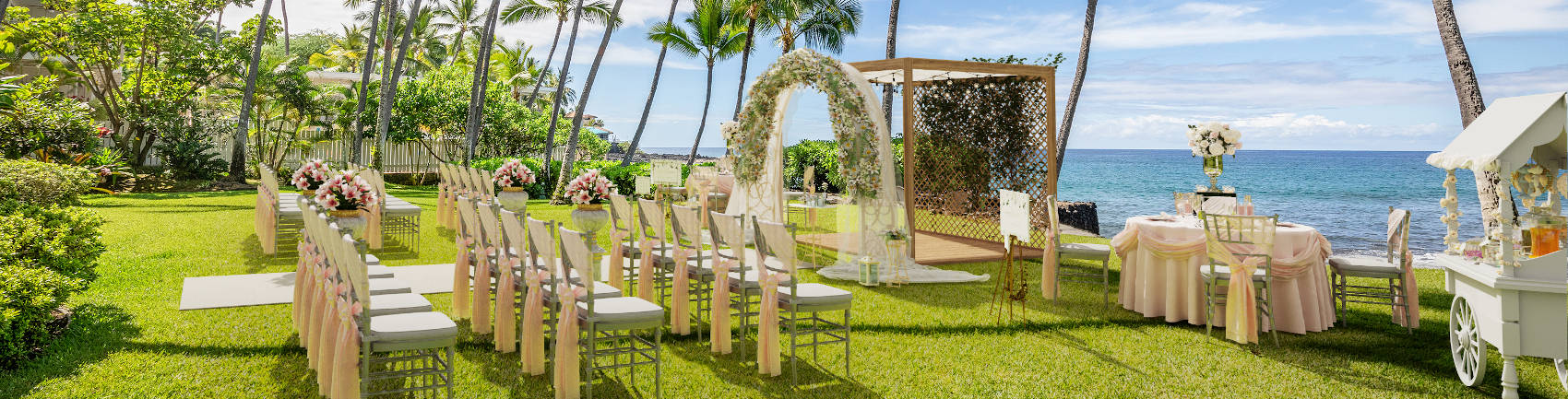 Wedding set up on the lawn with flowers lining the aisle and a flower adorned archway 