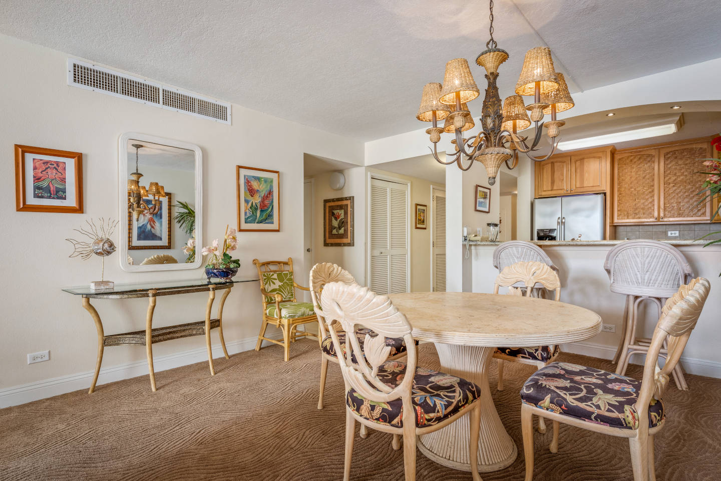 Dining area in the two bedroom ocean view unit with a round dining table and matching floral pattern chairs, mirror and a side table, bar stools facing the kitchen