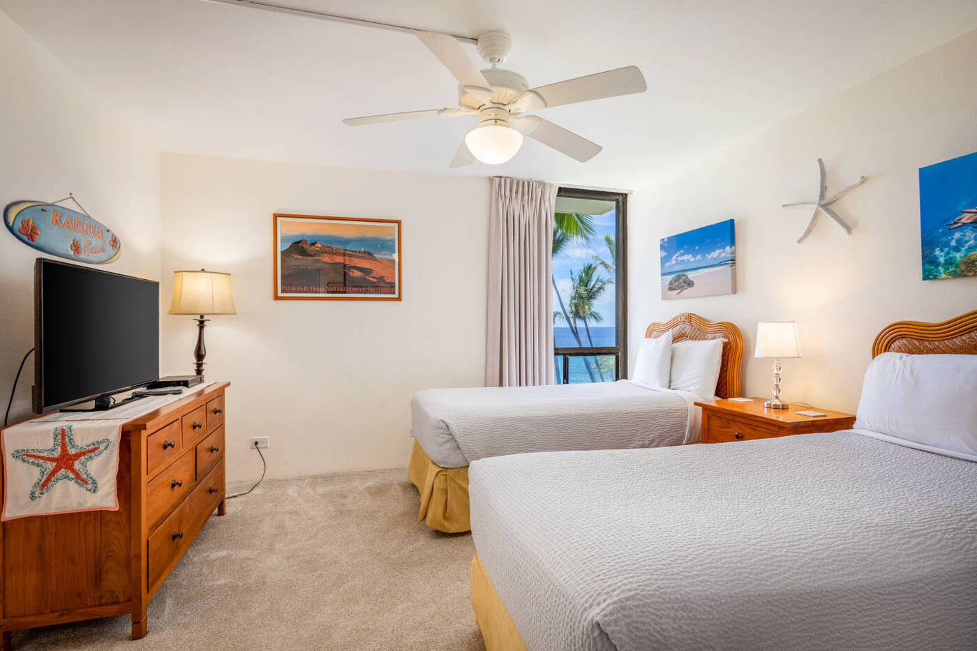 Twin beds in second guest room with pictures on the walls, flat screen TV, and a window overlooking to beach 