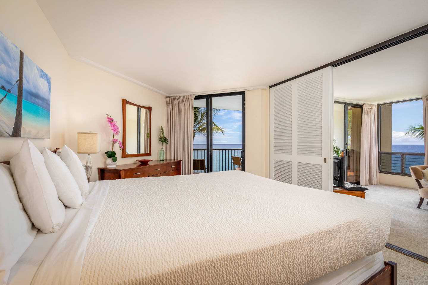 Master bedroom with king bed, dresser with orchid plant, balcony overlooking the ocean and sliding doors to living room