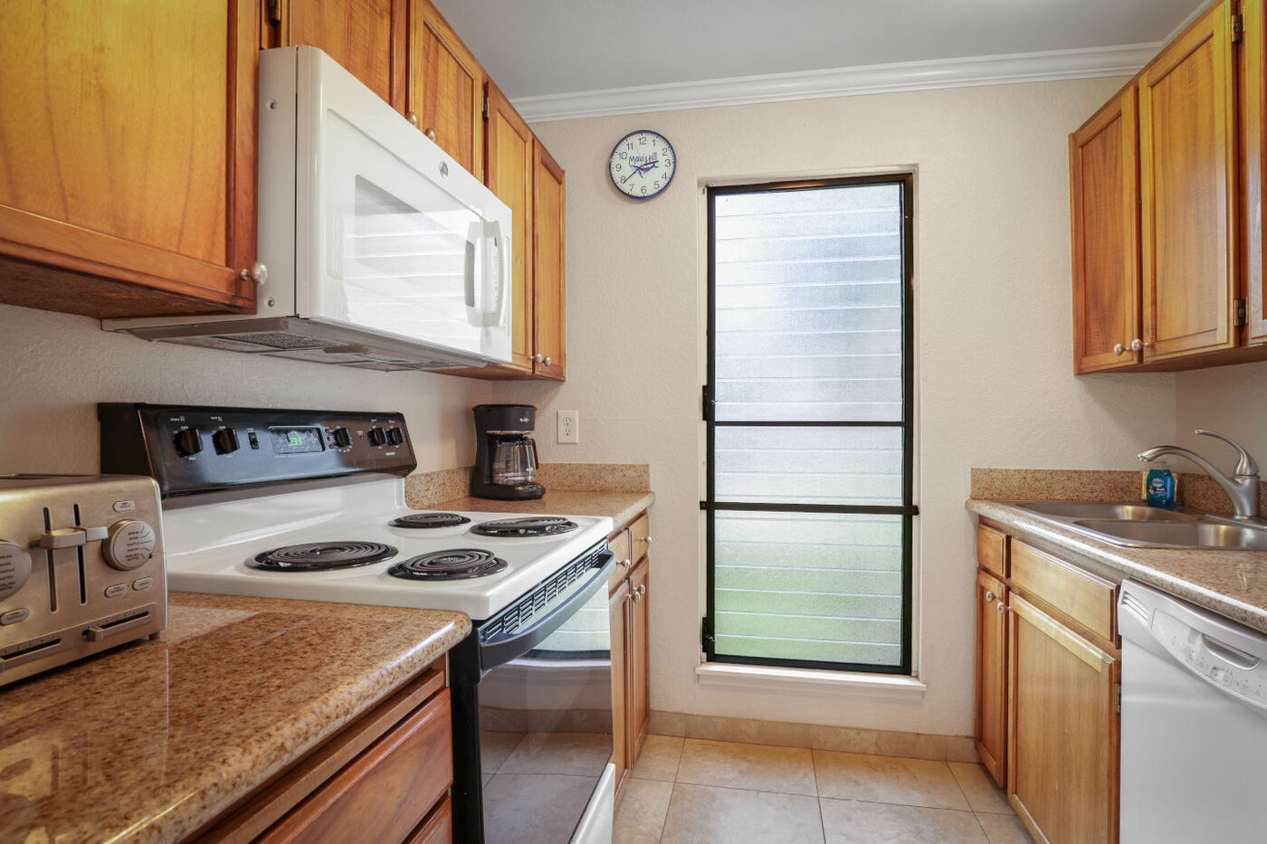 Full kitchen with a four-burner cooktop stove, marble countertops, microwave, coffee maker and toaster. 