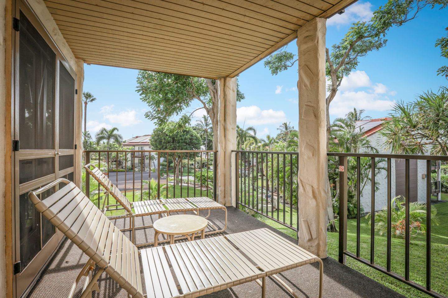 Covered lanai with railing, two outdoor lounge chairs and a table