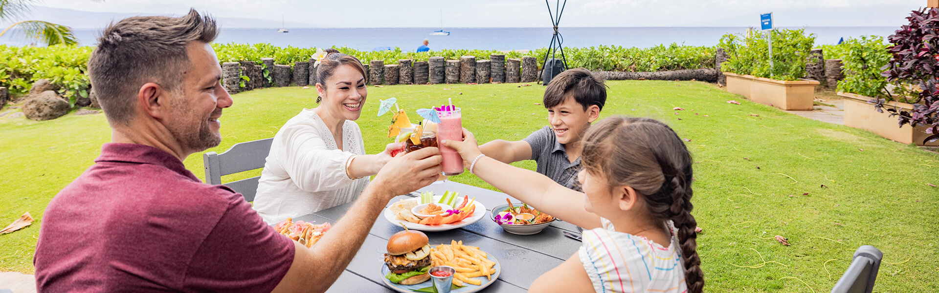 Family enjoying lunch and drinks outdoor restaurant with views of beach and neighbor island 