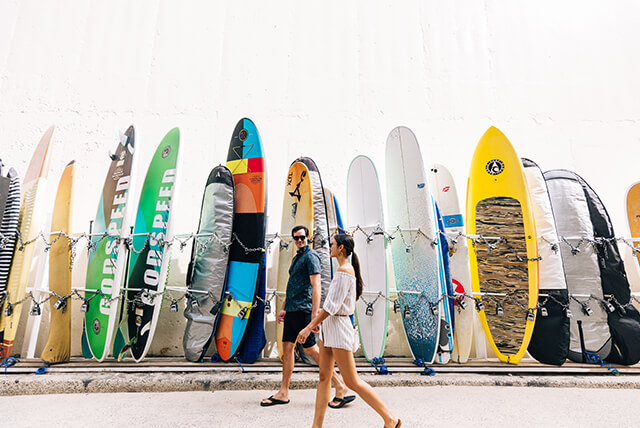 Couple walking along path with wall of surfboards