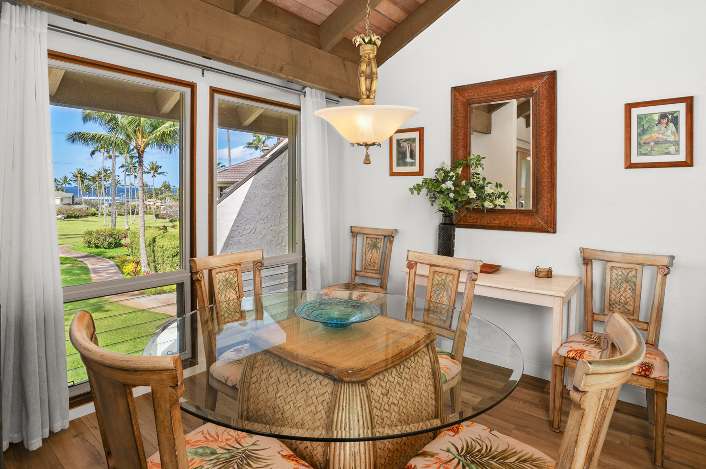 Dining area with table, chairs, and large windows with garden and ocean views in distance.