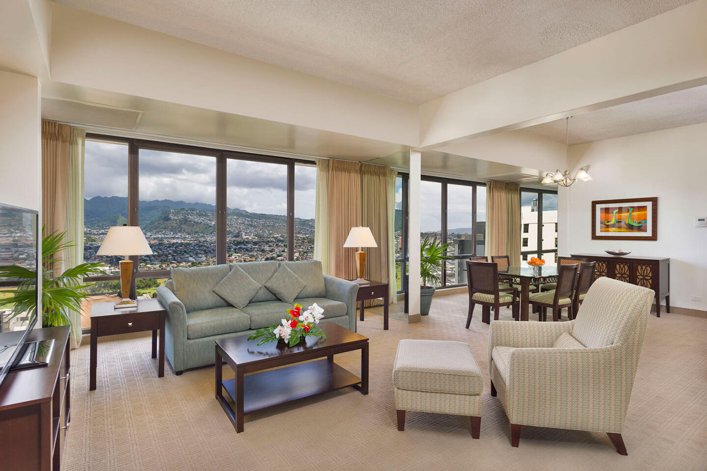 Living area with a couch, coffee table, TV, and large picture windows with mountain views.
