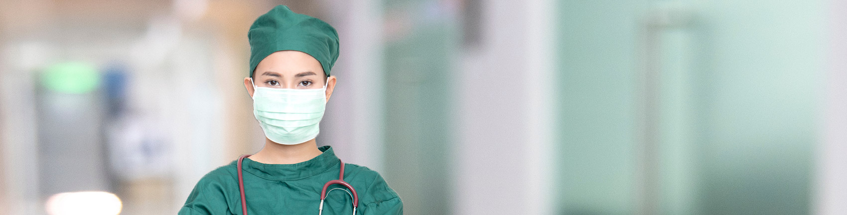 Medical worker wearing green scrubs and cap also wearing a face mask.