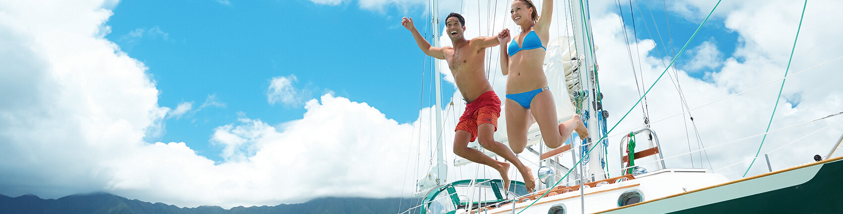 Male and female holding hands jumping into the water from the side of a boat