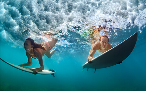 Two women diving under wave with surfboards