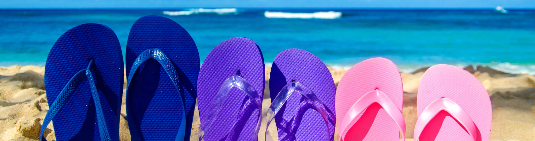 Blue, purple, pink slippers planted in the sand with blue waters in the background